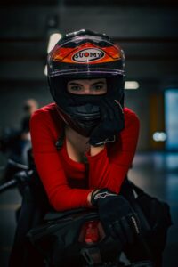 Confident female motorcyclist poses indoors with helmet.