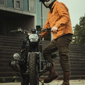 Man in orange jacket standing with motorcycle outdoors in Eindhoven, Netherlands.