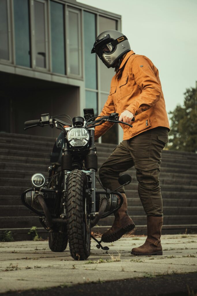 Man in orange jacket standing with motorcycle outdoors in Eindhoven, Netherlands.